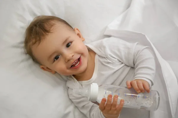 Симпатичный малыш с бутылкой, лежащий в удобной кроватке, вид сверху — стоковое фото