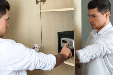 Otelde elektronik kilitle siyah çelik kasa açan adam.