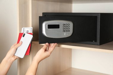Akıllı telefonu, pasaportu ve parayı çelik kasaya koyan kadın, yakın plan.