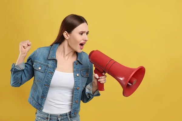 Mulher jovem emocional com megafone no fundo amarelo — Fotografia de Stock