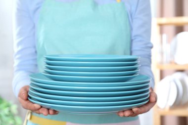 Kadın arka planda temiz tabak yığını tutuyor, kapat