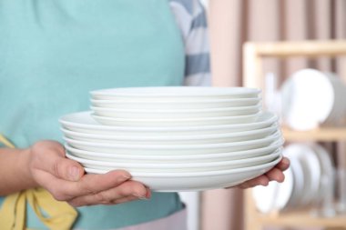 Kadın arka planda temiz tabak yığını tutuyor, kapat