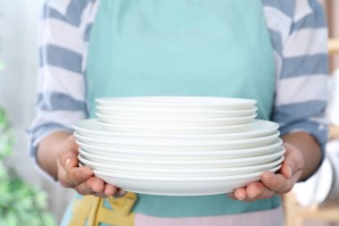 Kadın arka planda temiz tabak yığını tutuyor, kapat