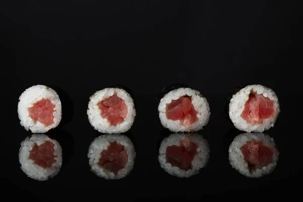 Delicious sushi rolls on black mirror surface