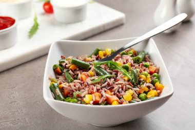 Tasty brown rice with vegetables on grey table