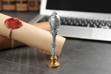 Noterin kalemi ve mühürlü belgeleri gri taş masadaki dizüstü bilgisayarın yanında.