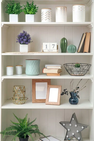 Bitkilerle dolu beyaz raf ünitesi ve farklı dekoratif malzemeler.