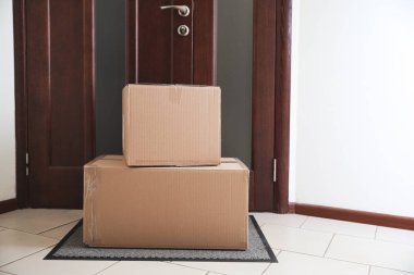Kapının yanındaki halıda karton kutular. Paket teslimat servisi