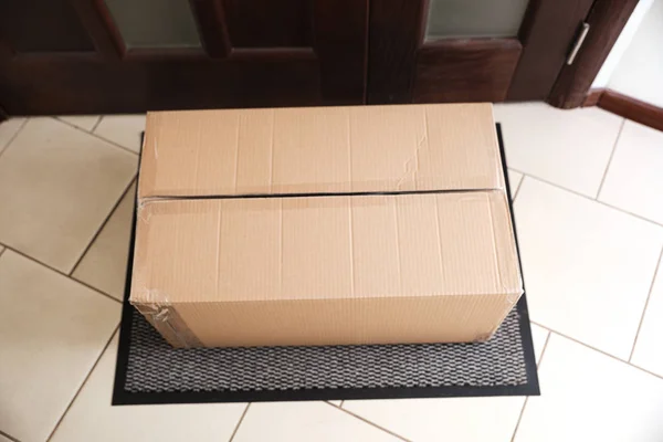 Caja de cartón en alfombra cerca de la puerta, por encima de la vista. Servicio de entrega de paquetes — Foto de Stock