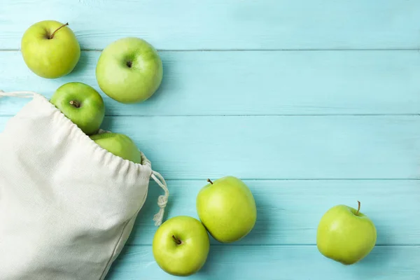 Cotton eco bag with apples on light blue wooden background, flat lay. Space for text