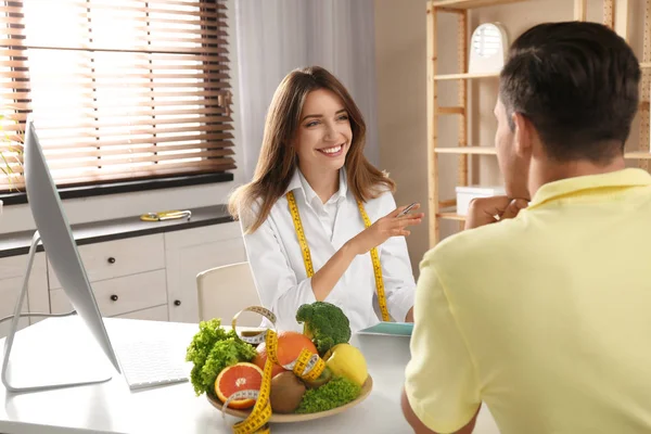 Young nutritionist consulting patient at table in clinic — 스톡 사진