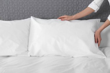 Woman fluffing soft pillow in bedroom, closeup