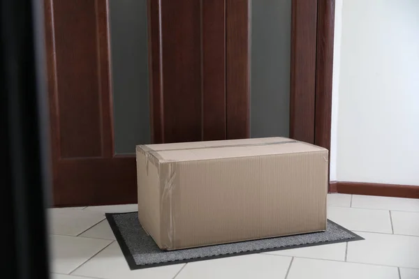 Caixa de papelão no tapete perto da porta. Serviço de entrega de encomendas — Fotografia de Stock