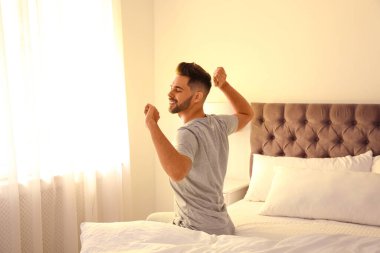 Young man stretching on bed at home. Lazy morning