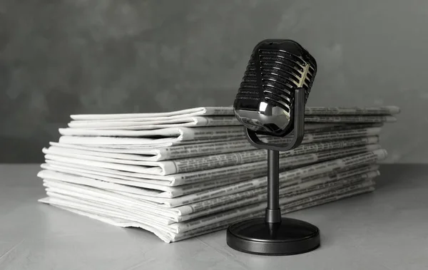 Newspapers and vintage microphone on light grey stone table. Jou