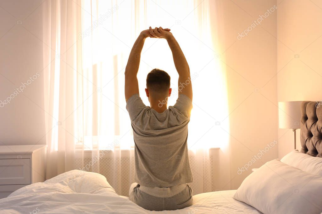 Young man stretching on bed at home, view from back. Lazy morning