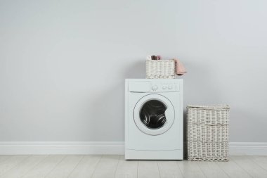Modern washing machine with laundry baskets near white wall. Spa