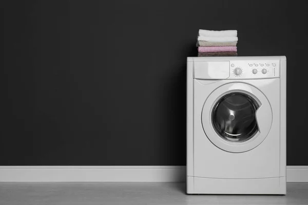 Moderní pračka s hromadou ručníků u černé stěny, lázně — Stock fotografie