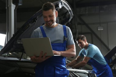 Mechanic with laptop doing car diagnostic at automobile repair s
