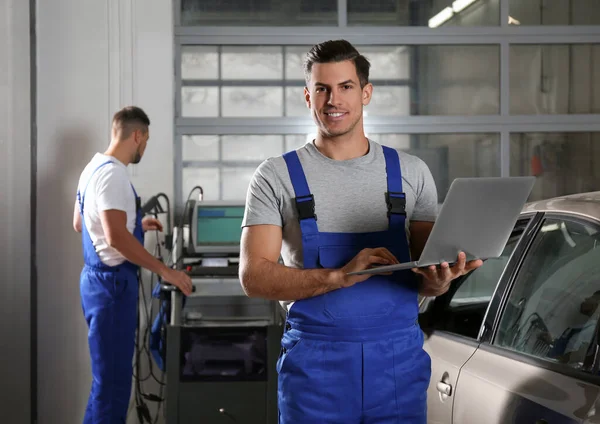 Mechanic with laptop doing car diagnostic at automobile repair s — Stok fotoğraf