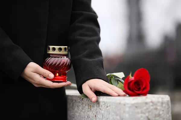 Woman holding candle near grey granite tombstone outdoors, close — Stockfoto