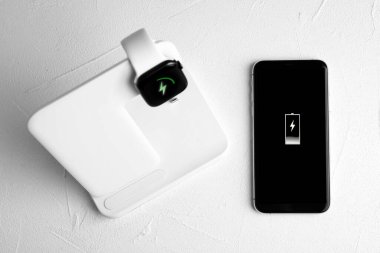Smartwatch charging with wireless pad and mobile phone on white 