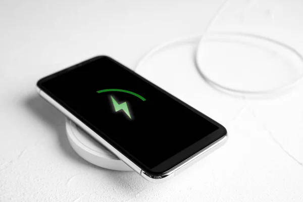 Зарядка мобильного телефона с беспроводной площадкой на белом каменном столе — стоковое фото