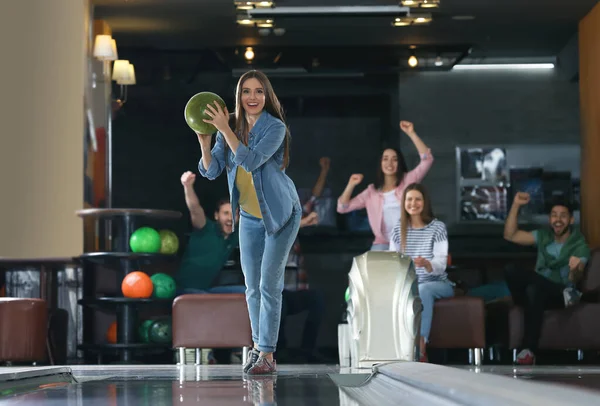 Genç bir kadın top oynuyor ve arkadaşlarıyla bowling kulübünde vakit geçiriyor.