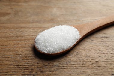 Spoon of white sugar on wooden table, closeup