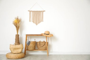 Stylish room with wooden table and wicker bags near white wall, 