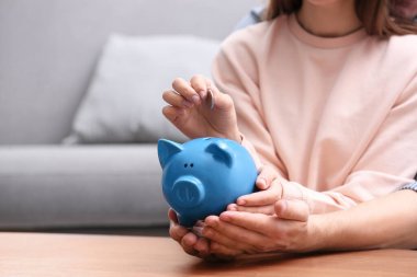 Couple with piggy bank and coin at wooden table, closeup