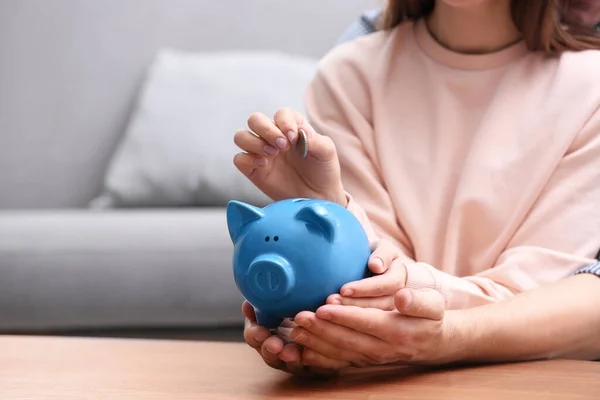 Couple with piggy bank and coin at wooden table, closeup — 스톡 사진