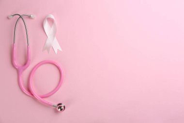 Göğüs kanseri farkındalığı sembolü olarak pembe kurdele ve arka planda steteskop, düz konum. Metin için boşluk