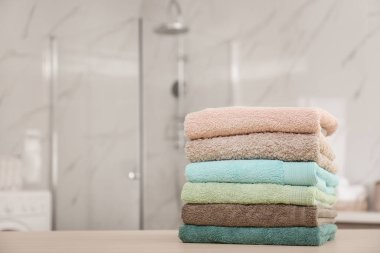 Stack of fresh towels on wooden table in bathroom. Space for tex