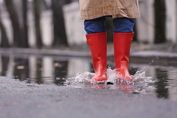 Woman in rubber boots jumping over puddle on rainy day, closeup. — ストック写真