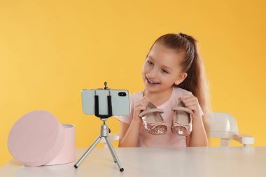 Sarı arka plandaki masada ayakkabılarını kaydeden şirin bir blogcu.