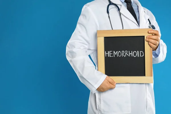Doctor Sosteniendo Pizarra Con Palabra Hemorrhoid Sobre Fondo Azul Primer — Foto de Stock