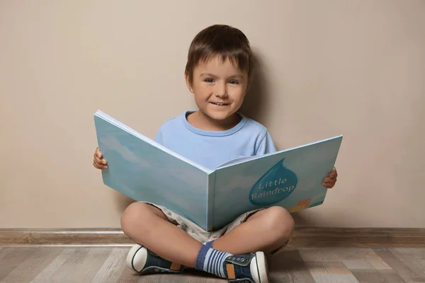かわいい男の子読書本で床の近くベージュの壁 — ストック写真