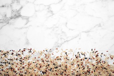 Mix of brown rice on marble table, top view. Space for text
