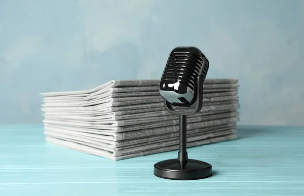 Newspapers and vintage microphone on light blue wooden table. Jo