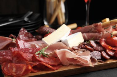 Tasty prosciutto with other delicacies served on black table, closeup