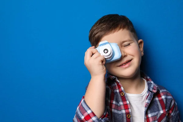 Маленький фотограф фотографирует с игрушечной камерой на голубом фоне — стоковое фото