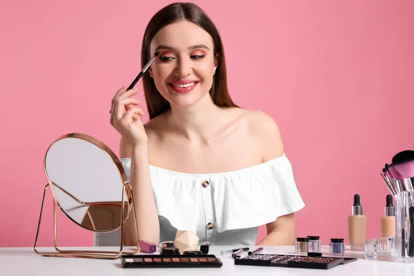 Beauty blogger applying eyeshadow on pink background