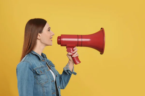 Jovem mulher com megafone no fundo amarelo — Fotografia de Stock