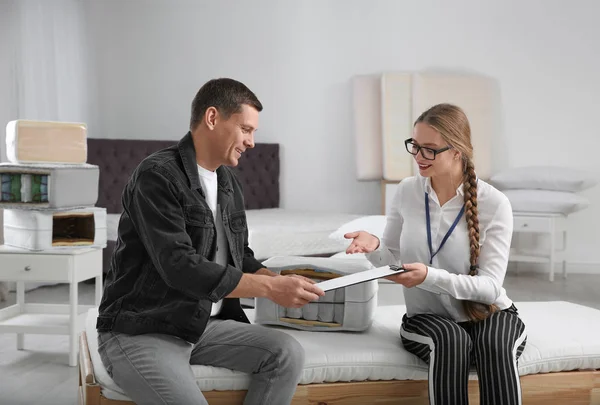 Young saleswoman consulting man in mattress store — Stok fotoğraf