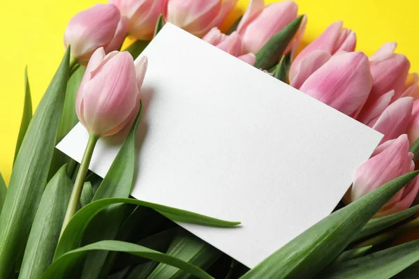 Hermosos tulipanes rosados de primavera y tarjeta en blanco sobre fondo amarillo — Foto de Stock
