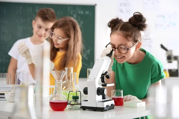 Школьница смотрит через микроскоп на своих одноклассников — стоковое фото