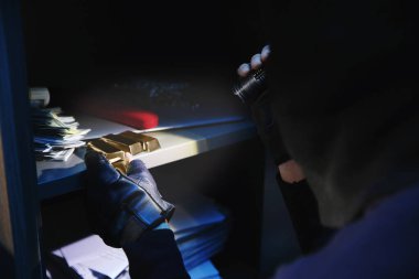 Thief taking gold bars out of steel safe indoors at night, closeup
