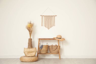 Stylish room with wooden table and wicker bags near white wall. 