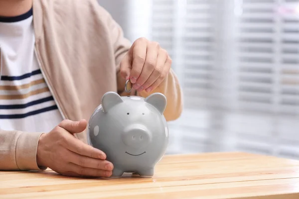 Hombre poniendo moneda en alcancía en la mesa de madera, primer plano. Espacio — Foto de Stock